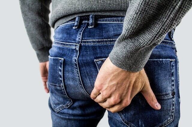 Picture of a man in Jeans holding his glutes due to the pain from Hemorrhoids